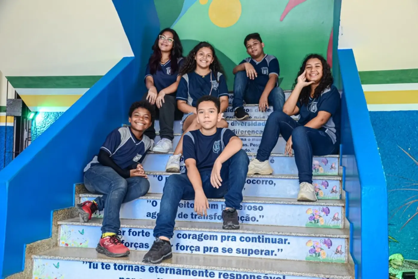 Estudantes uniformizados reunidos em escadaria de escola.