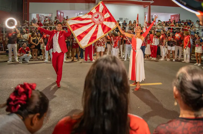 Casal de mestre-sala e porta-bandeira se apresenta diante do público durante atividade de escola de samba no Amapá.
